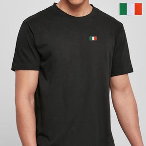 May include: A black short-sleeved t-shirt featuring a small, rectangular Italian flag patch embroidered on the left chest. The garment has a classic crew neckline and a straight hem, providing a clean and simple look for everyday wear.