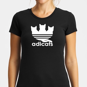 May include: Black t-shirt with a white graphic of three cats forming a stylized Adidas logo. The text "adicats" is below the logo.