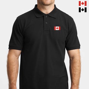 Puede incluir: Polo negro con un parche de la bandera canadiense roja y blanca en el pecho. La bandera presenta una hoja de arce roja sobre un cuadrado blanco, con barras rojas a cada lado. La camisa tiene cuello y mangas cortas.