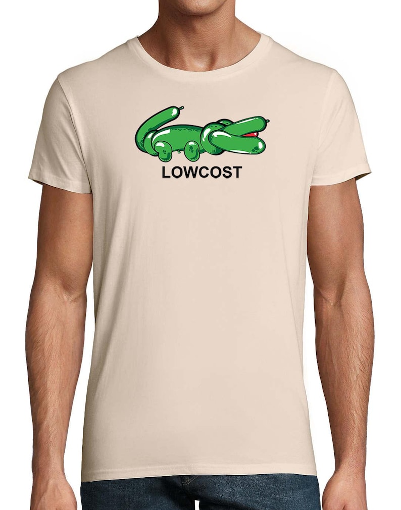 May include: Beige t-shirt featuring a green cartoon alligator design with the word "LOWCOST" in black text below. The alligator has a balloon-like appearance with red accents on its mouth.