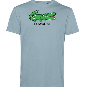 May include: Light blue t-shirt featuring a green cartoon alligator design with the word "LOWCOST" printed below. The alligator has a red mouth and is made to look like a balloon animal. The shirt is a short-sleeved crew neck.