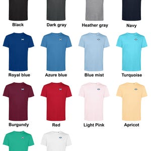 Op de afbeelding: Een collectie t-shirts met korte mouwen in diverse kleuren, waaronder zwart, grijs, blauw, rood en roze. Elk shirt heeft een klein geborduurd ontwerp op de borst. De beschikbare kleuren staan eronder.