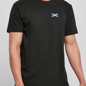 Op de afbeelding: Zwart T-shirt met ronde hals en een klein wit en blauw embleem op de linkerbovenborst. Het embleem heeft een witte 'X' over een blauwe rechthoek. Het T-shirt heeft korte mouwen.
