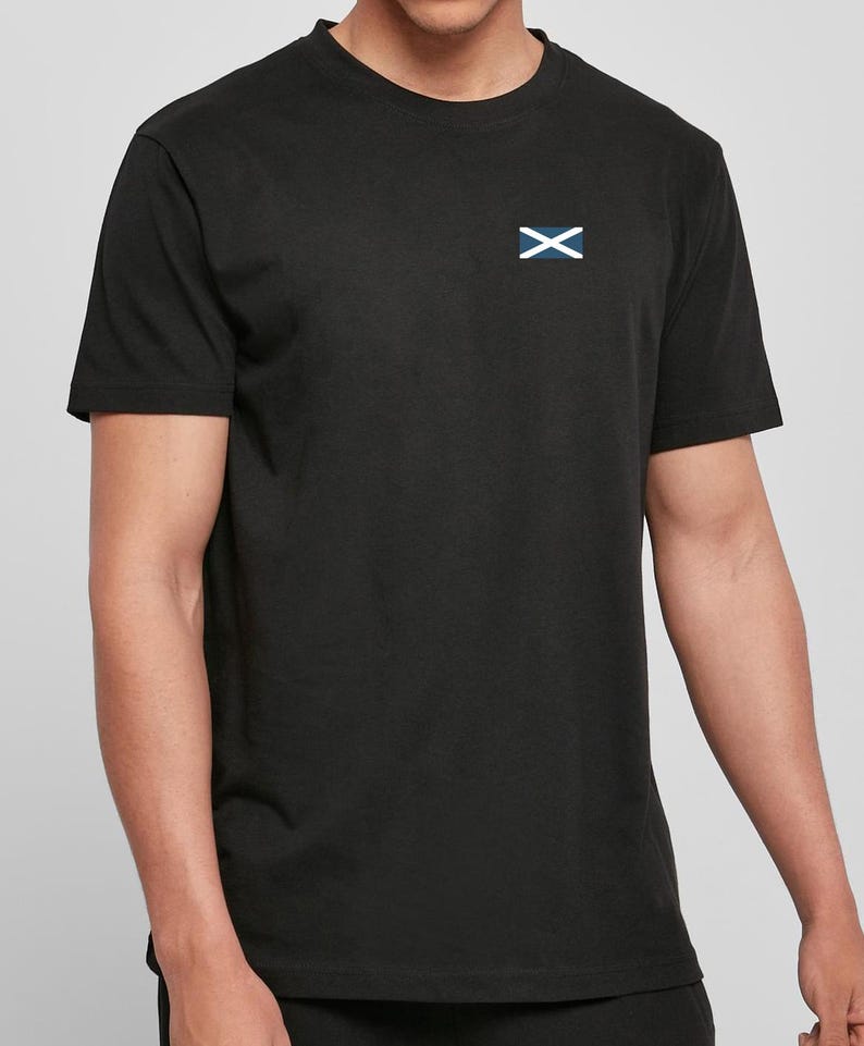 Op de afbeelding: Zwart T-shirt met ronde hals en een klein wit en blauw embleem op de linkerbovenborst. Het embleem heeft een witte 'X' over een blauwe rechthoek. Het T-shirt heeft korte mouwen.