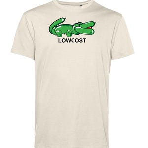 May include: A light beige t-shirt featuring a green cartoon alligator design with the word "LOWCOST" in black text. The alligator has a red mouth and is positioned on the front of the shirt. The shirt has short sleeves.