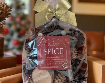 May include: A clear cellophane bag filled with a holiday potpourri blend. The bag is tied with a gold bow. A label reads "High Rock Candle Co. SPICE" with "Cinnamon Stick" and "Holiday Blend" text. The bag contains pine cones, wood slices, and cinnamon sticks.