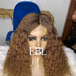 May include: A brown and blonde braided wig with a lace front. The wig has a natural-looking hairline and a full, curly texture. The text "EBL" is visible on the wig.