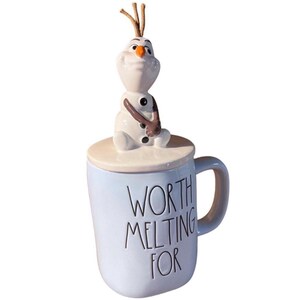 May include: A blue ceramic mug with a white lid featuring a snowman figurine. The mug has the text "Worth Melting For" printed on the front.