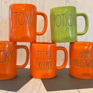 Op de afbeelding: Vijf keramische Halloween-mokken in oranje en groen. Elke mok heeft een ander woord in zwarte letters: "TOXIC", "POTION", "SPOOKY", "JEEPERS CREEPERS" en "HAPPY HALLOWEEN". De mokken hebben grote handvatten.