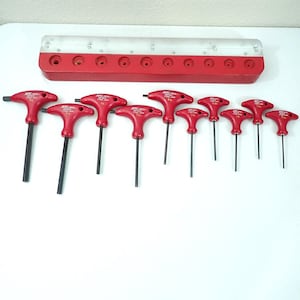 May include: A set of ten T-handle hex keys with red handles and black metal shafts, arranged in descending order of size. Each tool features the text MRC TOOLS and JAPAN. A red metal storage rack with ten circular slots is positioned above the tools.