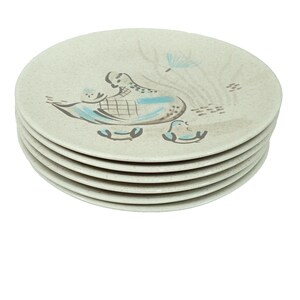 May include: A stack of five round, off-white speckled plates. Each plate features a stylized graphic of a bird with blue and brown accents, accompanied by a small bird figure and abstract line patterns in the background, creating a cohesive set.