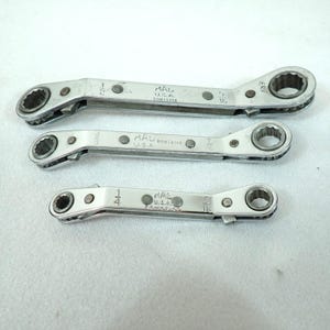 May include: Three silver-colored metal ratcheting wrenches of varying sizes, each marked with MAD U.S.A. and specific fractional measurements including 1/2, 5/16, 3/8, 7/16, 1/4, and 5/16 inches. These tools feature a dual-ended design with gear mechanisms.