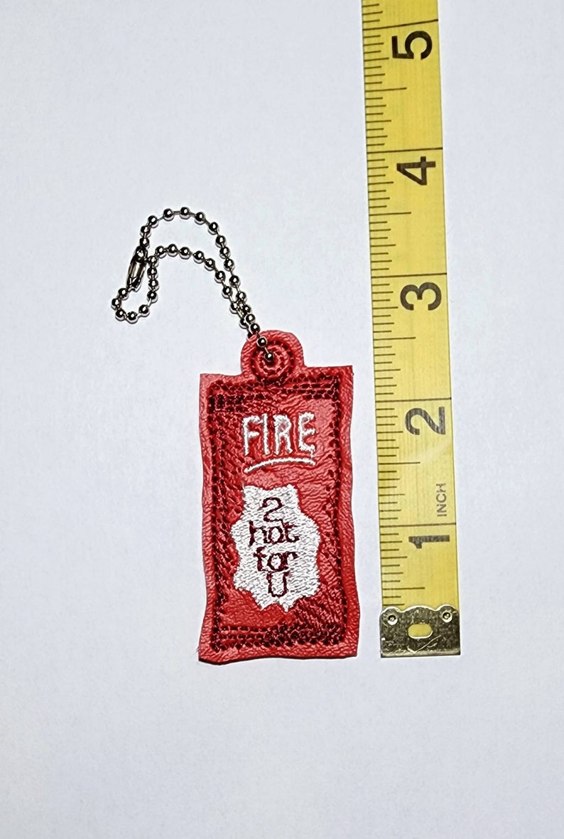 Puede incluir: Llavero de cuero rojo con un dise&ntilde;o bordado en blanco que dice "FIRE 2 hot for u".
