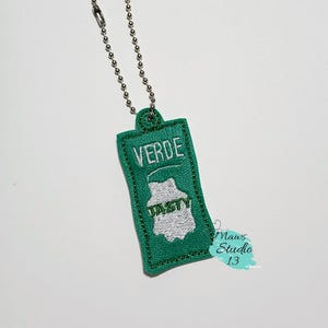 Puede incluir: Un llavero de tela verde con un dise&ntilde;o bordado en blanco que dice "VERDE" y "TASTY". El llavero tiene una cadena plateada.