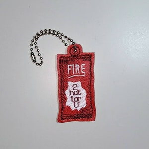 Puede incluir: Un llavero rojo con un dise&ntilde;o bordado en blanco que dice "FIRE 2 HOT FOR U".