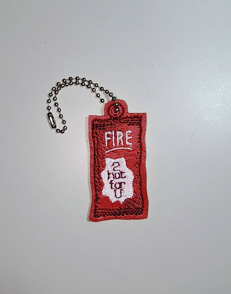 Puede incluir: Un llavero rojo con un dise&ntilde;o bordado en blanco que dice "FIRE 2 HOT FOR U".