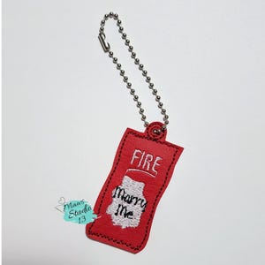 Puede incluir: Llavero de tela roja con forma de botella de salsa picante con las palabras "FIRE" y "Marry Me" bordadas.