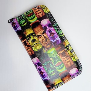May include: A zippered wallet featuring a collage of classic monster faces in vibrant colors. The design includes Frankenstein's monster, the Creature from the Black Lagoon, and other iconic horror characters. The wallet has a black border and a zipper closure.