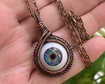May include: A copper wire wrapped pendant necklace with a blue and white glass eye charm.