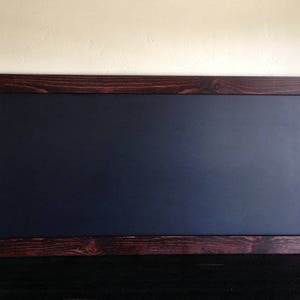 May include: A rectangular chalkboard with a dark blue surface and a stained, dark brown wooden frame. The frame has visible wood grain and knots. The chalkboard is displayed against a neutral-colored wall.