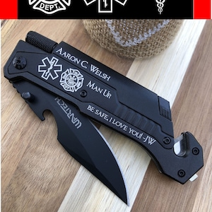 May include: Black multi-tool knife with a partially open blade. The knife features the Star of Life and Fire Department symbols, along with the text "AARON C. WELSH MAN UP. BE SAFE, I LOVE YOU! -JW". The brand name "UARTECH" is also visible.