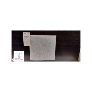 May include: A white square piece of Stabiliser, a type of fabric used for embroidery and quilting, on a dark wood surface. The label reads "Stabiliser Classic 5000 12 x 12"