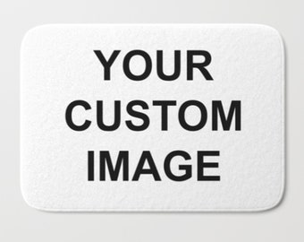 May include: White rectangular bath mat with rounded corners. The mat features the text "YOUR CUSTOM IMAGE" in bold black letters, centered on the surface. The background is a plain white.