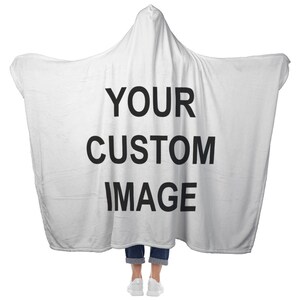 May include: A white hooded blanket with the text "YOUR CUSTOM IMAGE" in large black letters. The blanket is draped over a person wearing blue jeans and white sneakers. The blanket has a hood and wide sleeves.