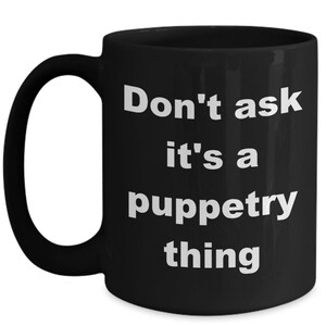 May include: Black ceramic mug with a white handle. The mug features the text "Don't ask it's a puppetry thing" in a bold, white font. The mug is designed for hot beverages and is suitable for home or office use.