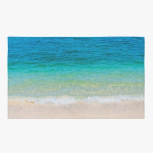May include: A serene beach scene with clear turquoise water gently lapping onto a white sandy shore. The water transitions from deep blue to light green, creating a gradient effect. A small wave is breaking on the beach.