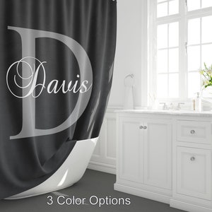 May include: A dark grey shower curtain featuring a large, light grey letter "D" and the name "Davis" in a script font. The text "3 Color Options" is at the bottom. The curtain is in a bathroom setting.