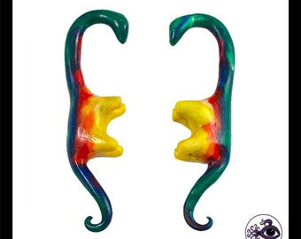 May include: Two colorful, abstract dinosaur-shaped earrings. The earrings are painted with a gradient of colors, including green, blue, red, and yellow. The design is whimsical and artistic, with a unique, handcrafted appearance.