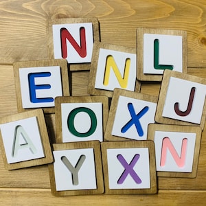 May include: Wooden tiles with the letters A, E, I, O, U, X, Y, N, J, and L in various colors. The tiles are arranged in a random pattern.
