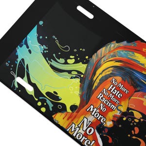 May include: Black luggage tag with a vibrant abstract design. The design includes a splash of blue and yellow paint, and a portrait with the words "No More Hate, No More Racism, No More!" printed in red and orange.