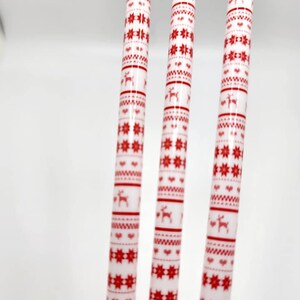 May include: Three white candles with a red and white Christmas pattern. The pattern includes snowflakes, hearts, and reindeer.