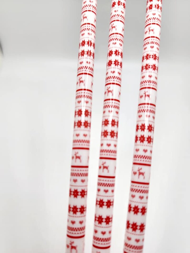 May include: Three white candles with a red and white Christmas pattern. The pattern includes snowflakes, hearts, and reindeer.