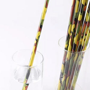 May include: A bundle of green, yellow, and brown camouflage patterned paper drinking straws in a clear glass. One straw is in a glass of water.