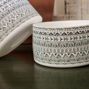 May include: Two white ceramic bowls with a black and white geometric pattern. The bowls are on a dark green surface.