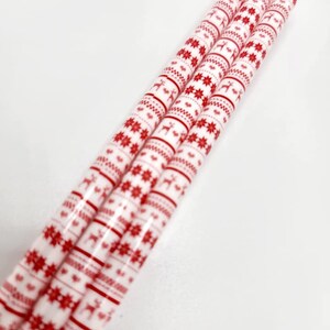 May include: Four red and white patterned paper straws with a Scandinavian Christmas design. The straws feature a repeating pattern of red snowflakes and reindeer on a white background.