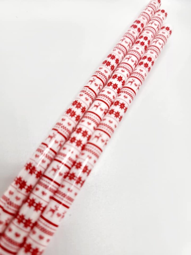 May include: Four red and white patterned paper straws with a Scandinavian Christmas design. The straws feature a repeating pattern of red snowflakes and reindeer on a white background.