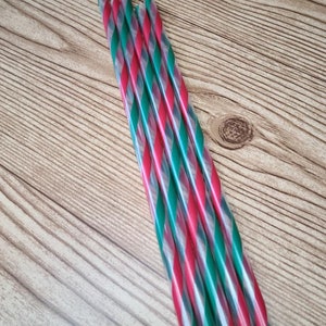 May include: A collection of red, green, and white striped plastic straws. The straws are arranged diagonally against a light brown wooden surface. The straws are transparent and appear to be for beverages.