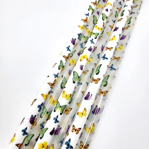 May include: A set of clear plastic drinking straws with a colorful butterfly pattern. The straws are arranged in a fan shape and are ready to be used for a fun and festive occasion.