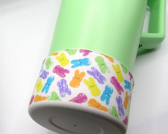May include: A green travel mug with a white band featuring a pattern of colorful Peeps marshmallow bunnies.