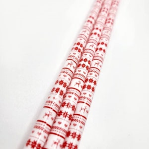 May include: Four white paper straws with a red and white Christmas pattern. The pattern includes snowflakes, reindeer, and stripes.