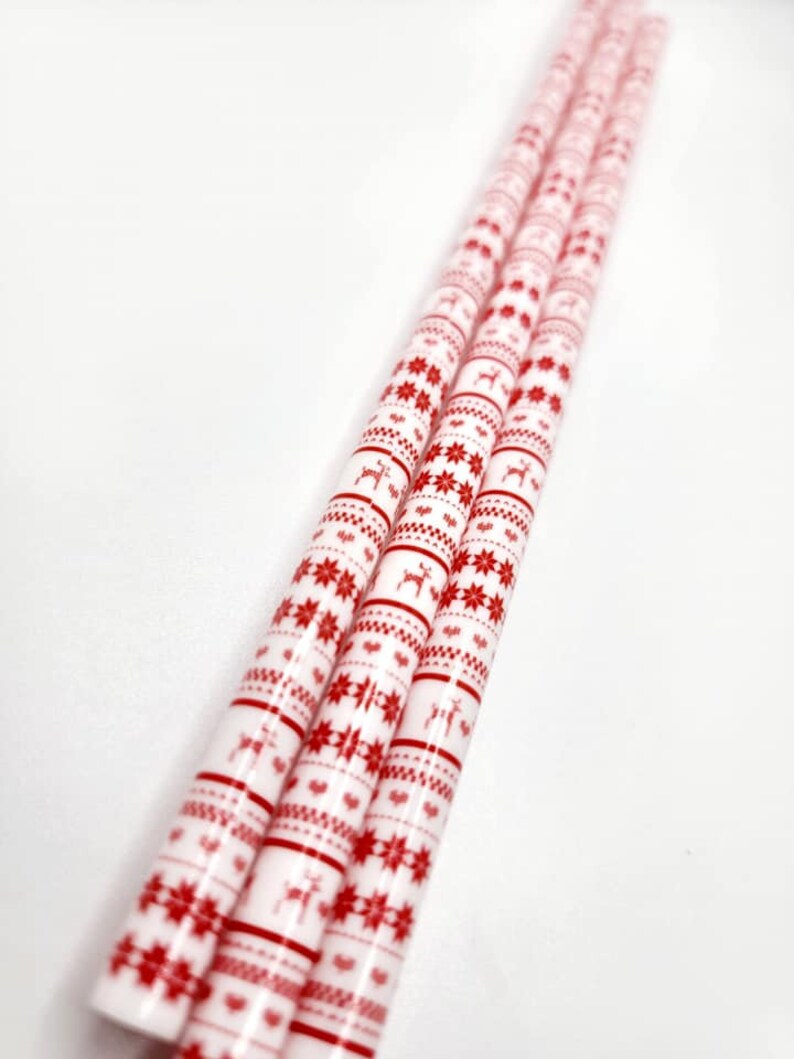 May include: Four white paper straws with a red and white Christmas pattern. The pattern includes snowflakes, reindeer, and stripes.