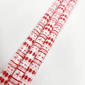 May include: Three white and red striped straws with a repeating pattern of snowflakes and reindeer. The straws are bundled together.
