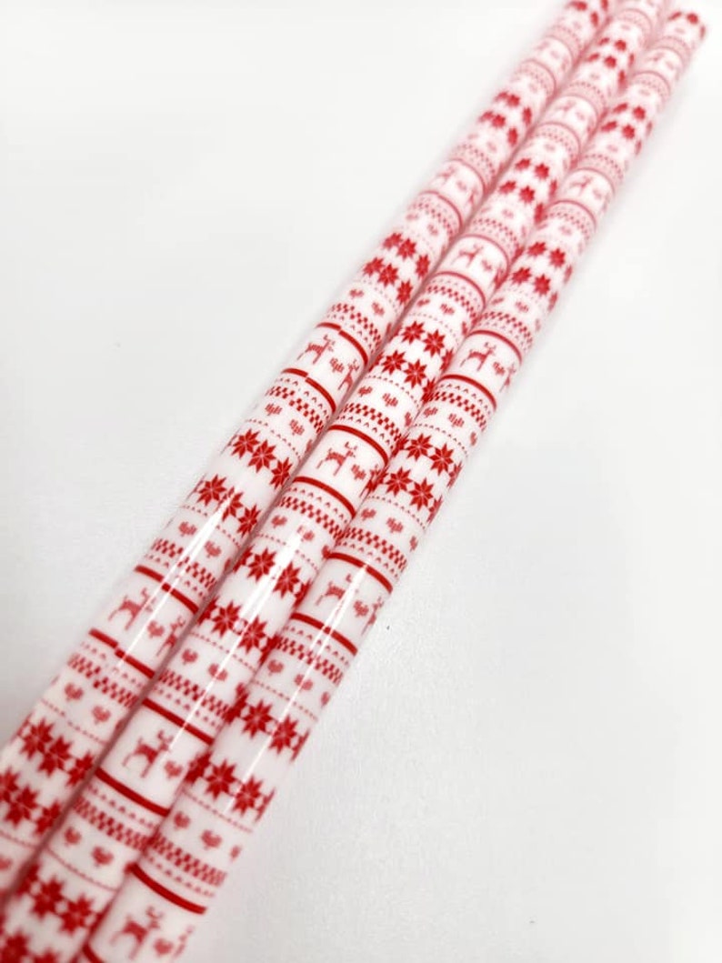 May include: Three white and red striped straws with a repeating pattern of snowflakes and reindeer. The straws are bundled together.