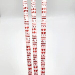 May include: Three white drinking straws with a red and white Christmas pattern. The pattern includes snowflakes, reindeer, and a geometric design.