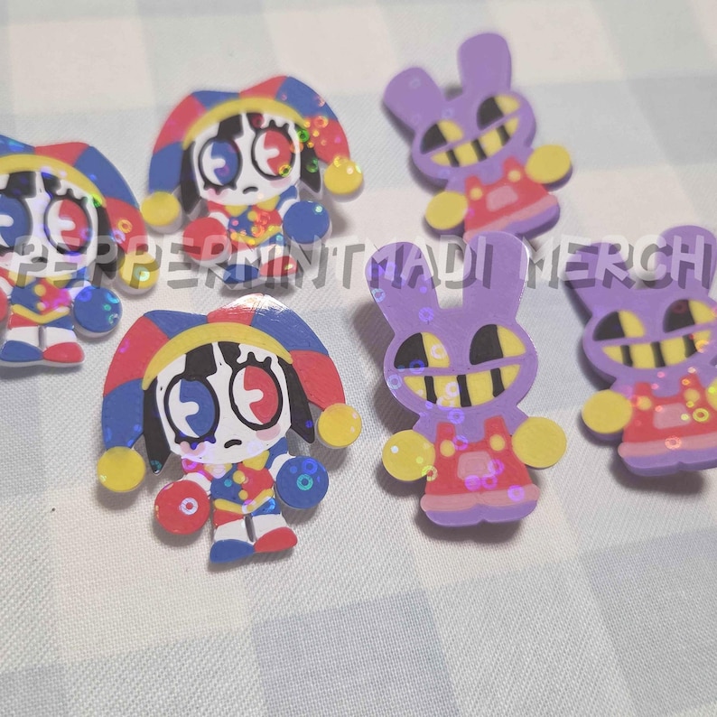 May include: A collection of colorful, cartoonish pins. Some pins feature a jester character with a red, blue, and yellow hat and outfit. Other pins are purple rabbits with yellow teeth and red overalls. The text "PEPPERMINT MADI MERCH" is visible.