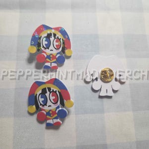 May include: Three decorative pins featuring a cartoon jester design. The jester pins have a red, blue, yellow, and white color scheme. One pin is a white silhouette with a gold pin back.